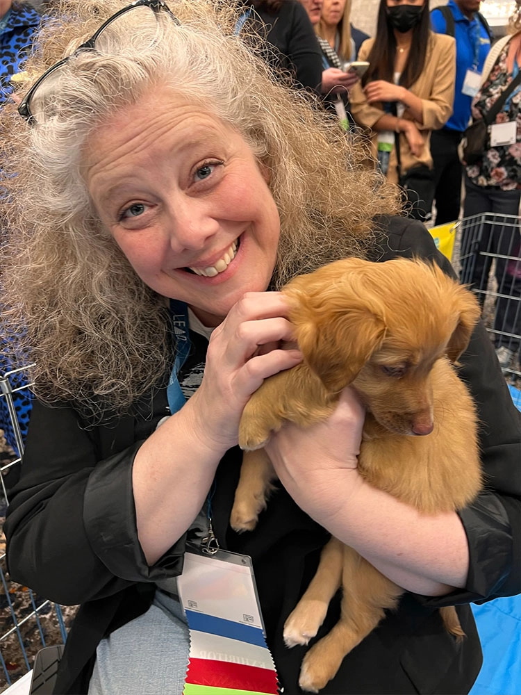A woman holding an adorable puppy at a puppy love™ puppy lounge!