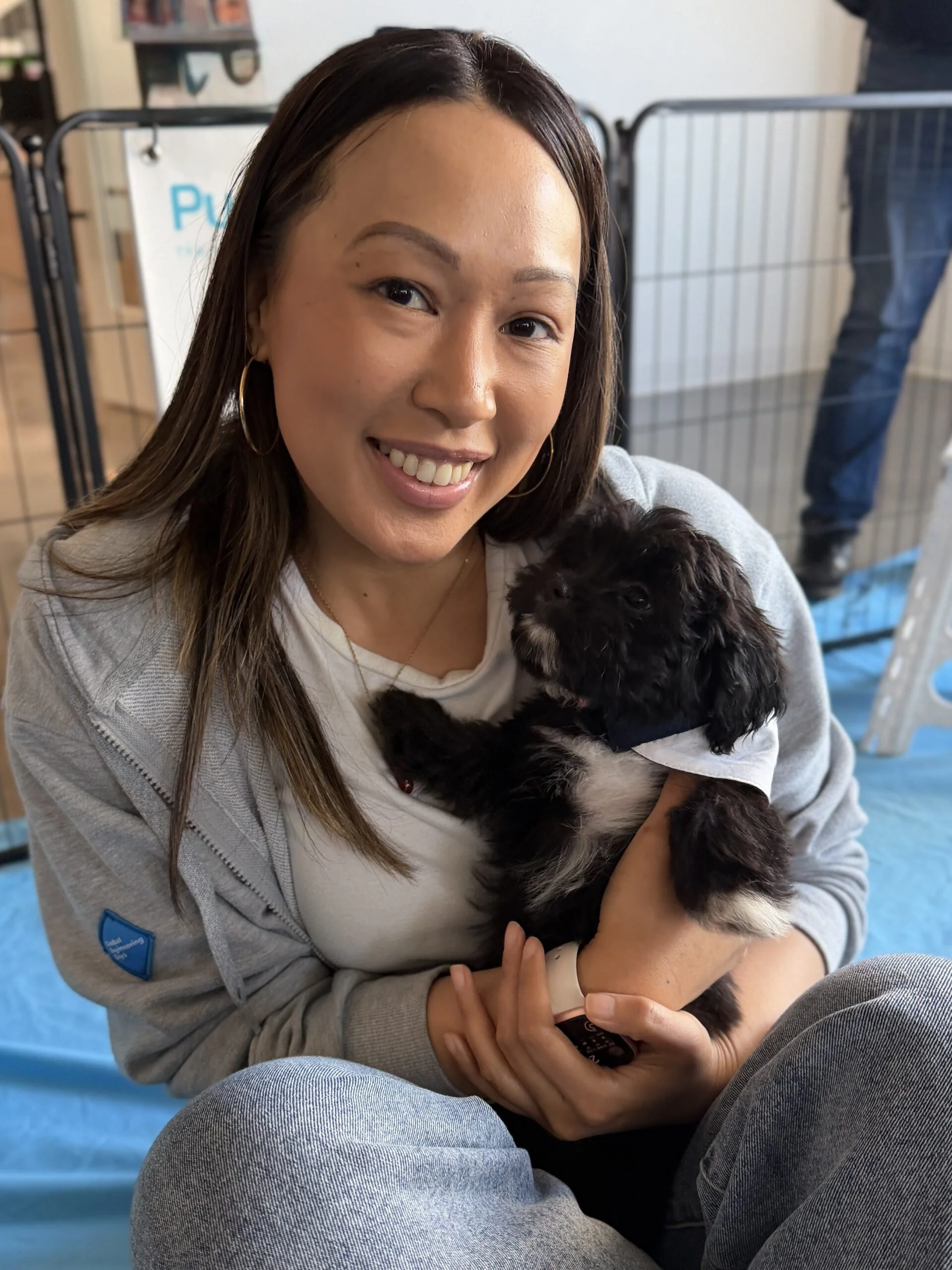 Smiling woman wearing a gray sweatshirt holding a small dark brown puppy