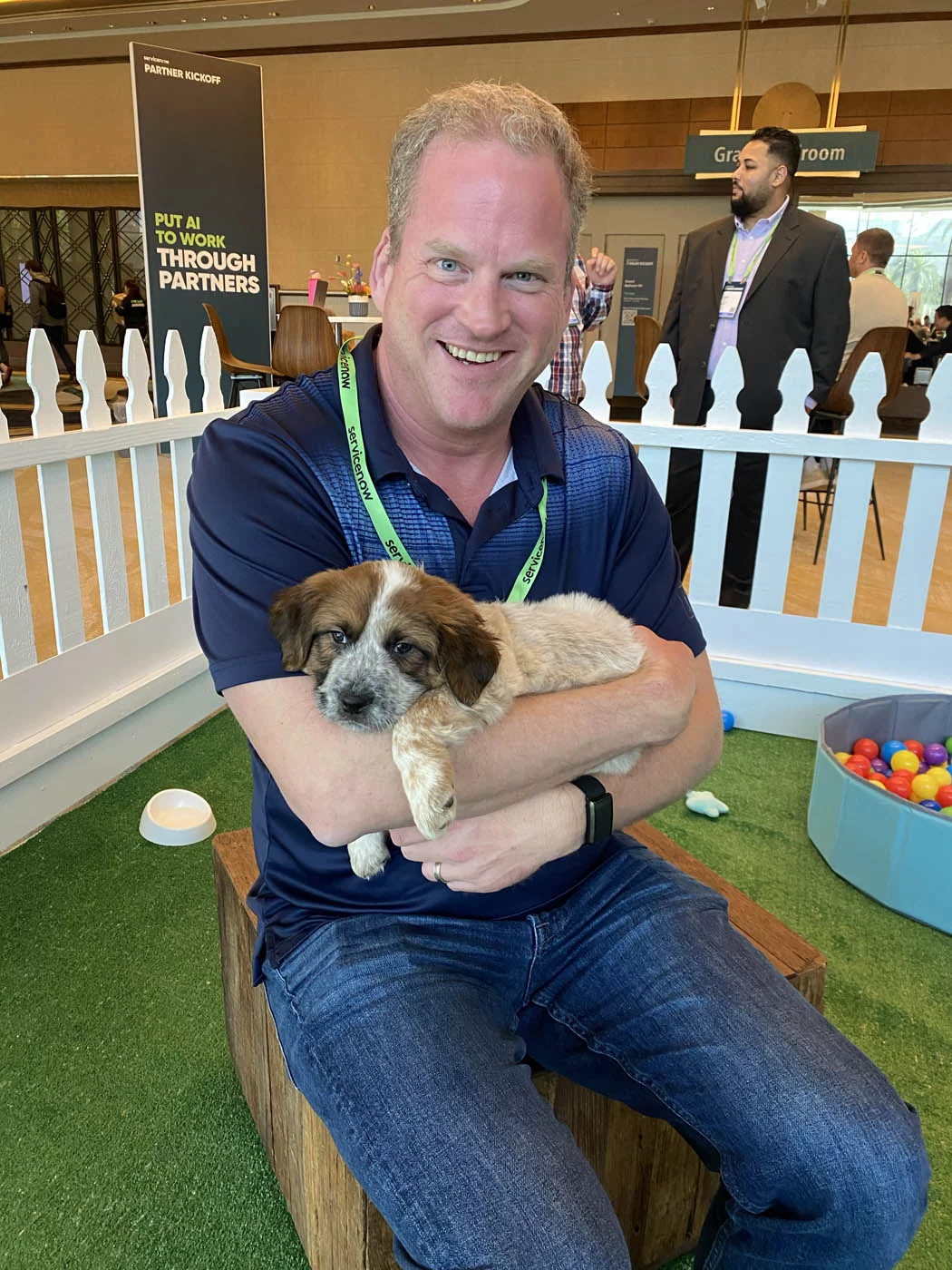 A man in a blue shirt holding a puppy and sitting down on a chair at their event with puppy love™.