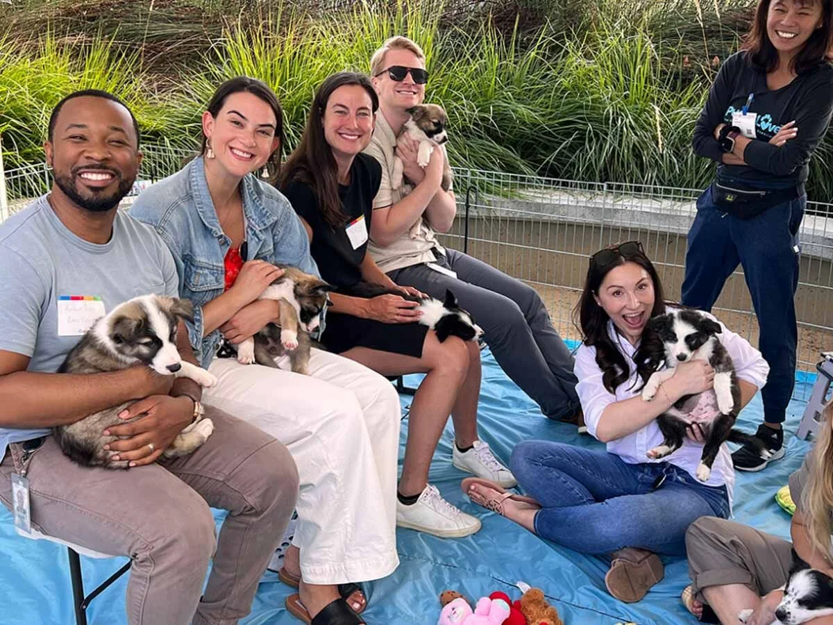 A women and man chatting at a puppy love™ event while holding a black pup.