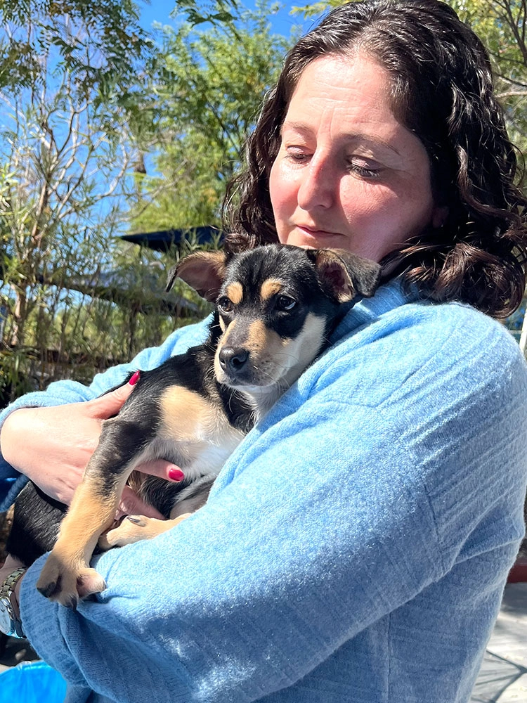 A woman in a blue shirt holding a puppy and smiling - feeling the benefits of adding puppy love™ to their company wellness programs.