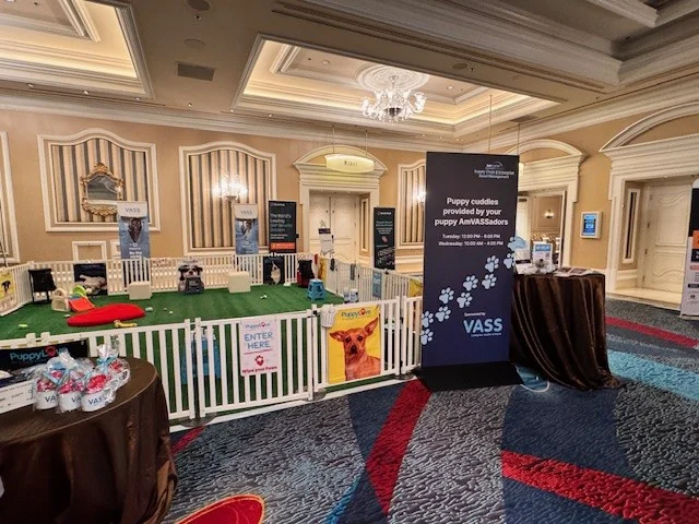 Puppy love™ corporate puppy therapy event setup at a conference venue with a fenced puppy play area and welcome booth.