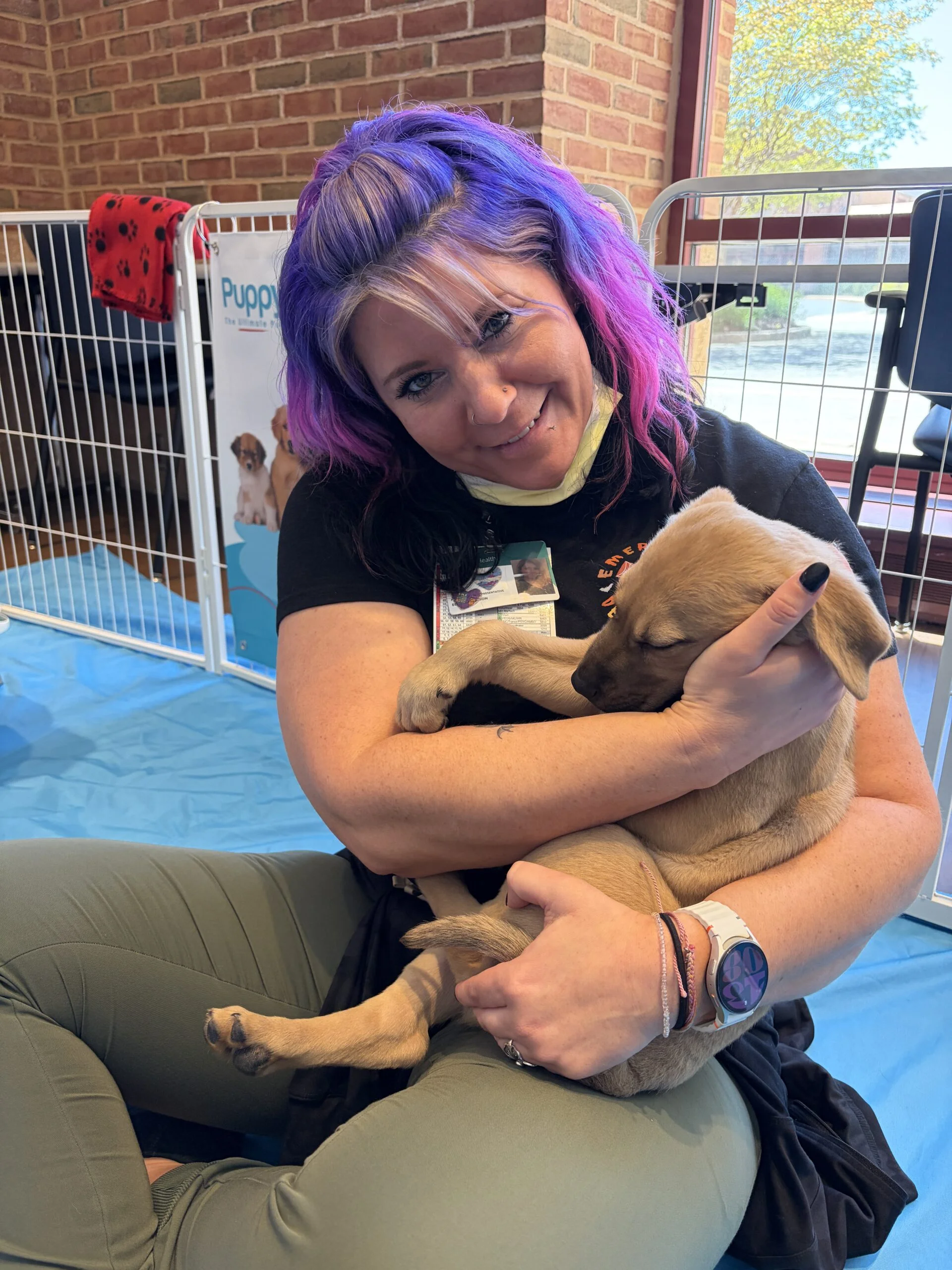 Woman with purple hair smiling while holding a tan puppy at luminis health aamc.