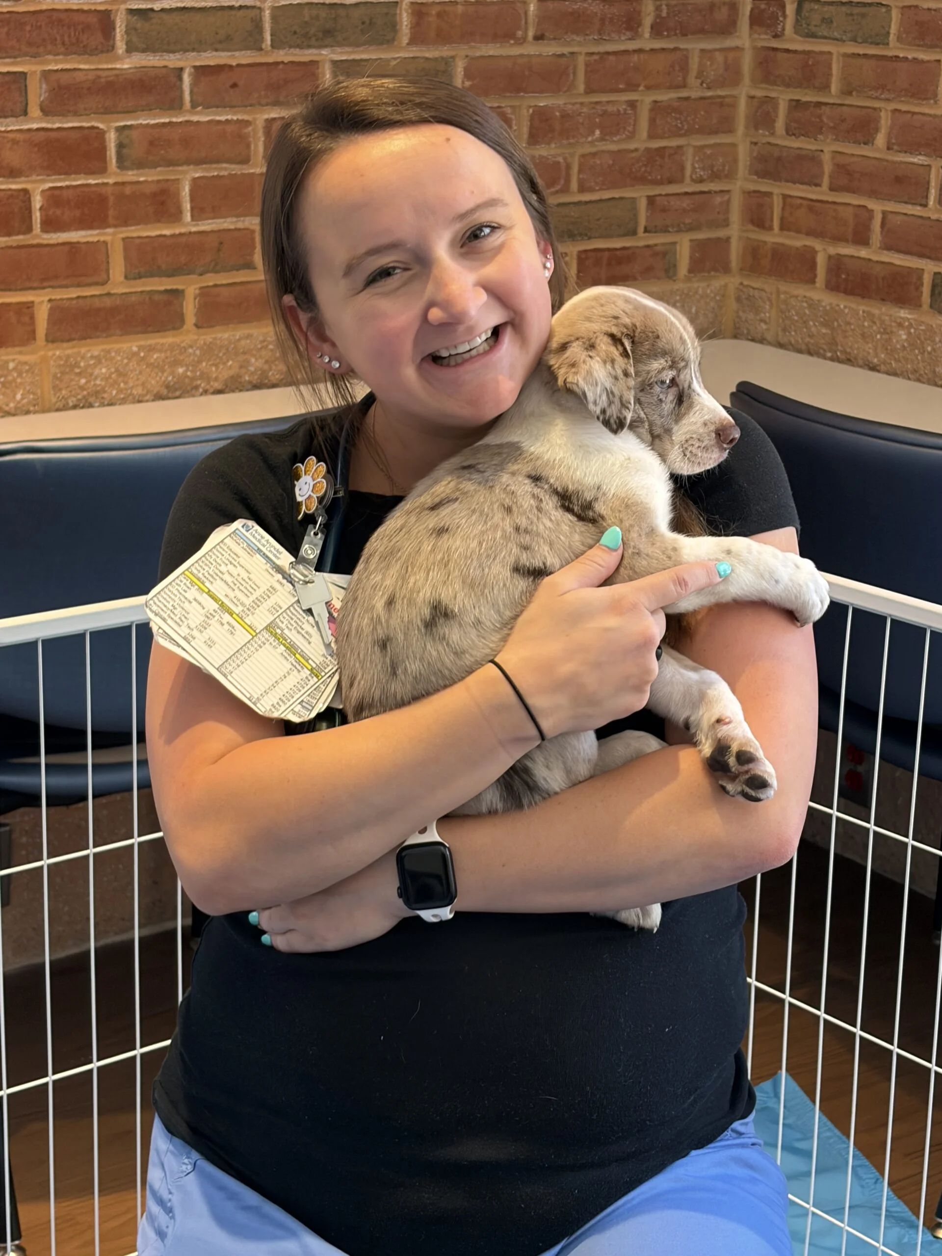Woman in a black top smiling while holding a speckled brown and white puppy at luminis health aamc.