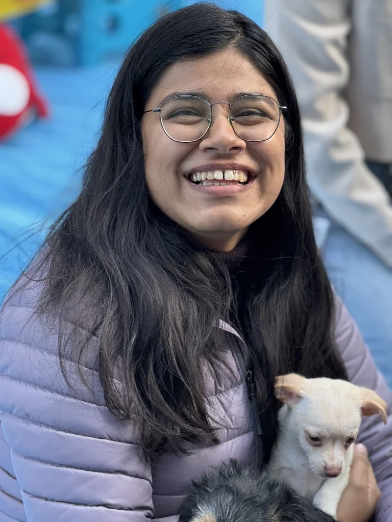 Smiling woman with dark hair and glasses holding a small white and tan puppy.